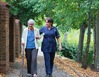 Nurse walking with elderly woman with a cane.